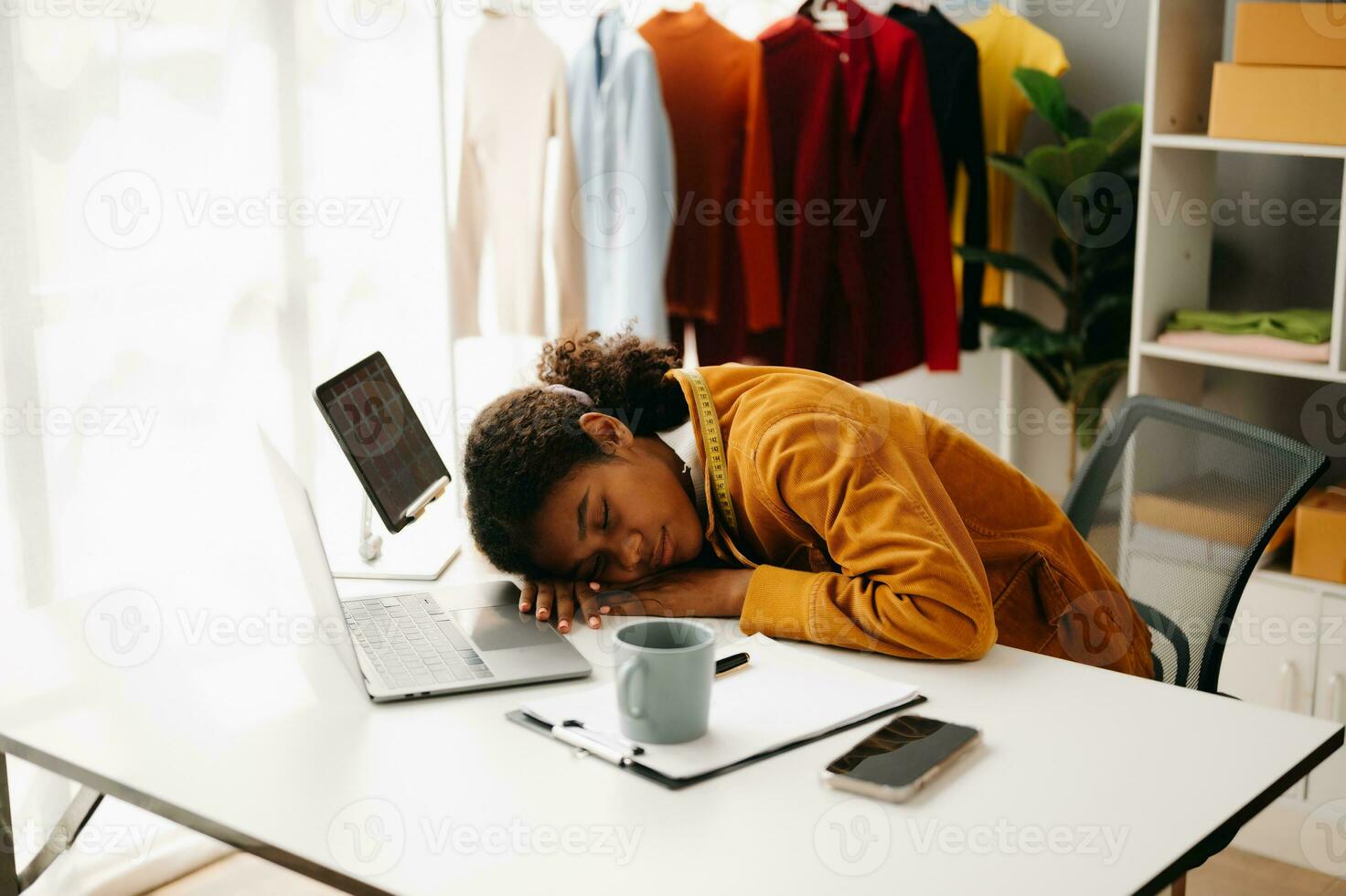 Calm curly brunette dark skinned woman on desk in office of fashion designer and holds tablet and smartphone. photo