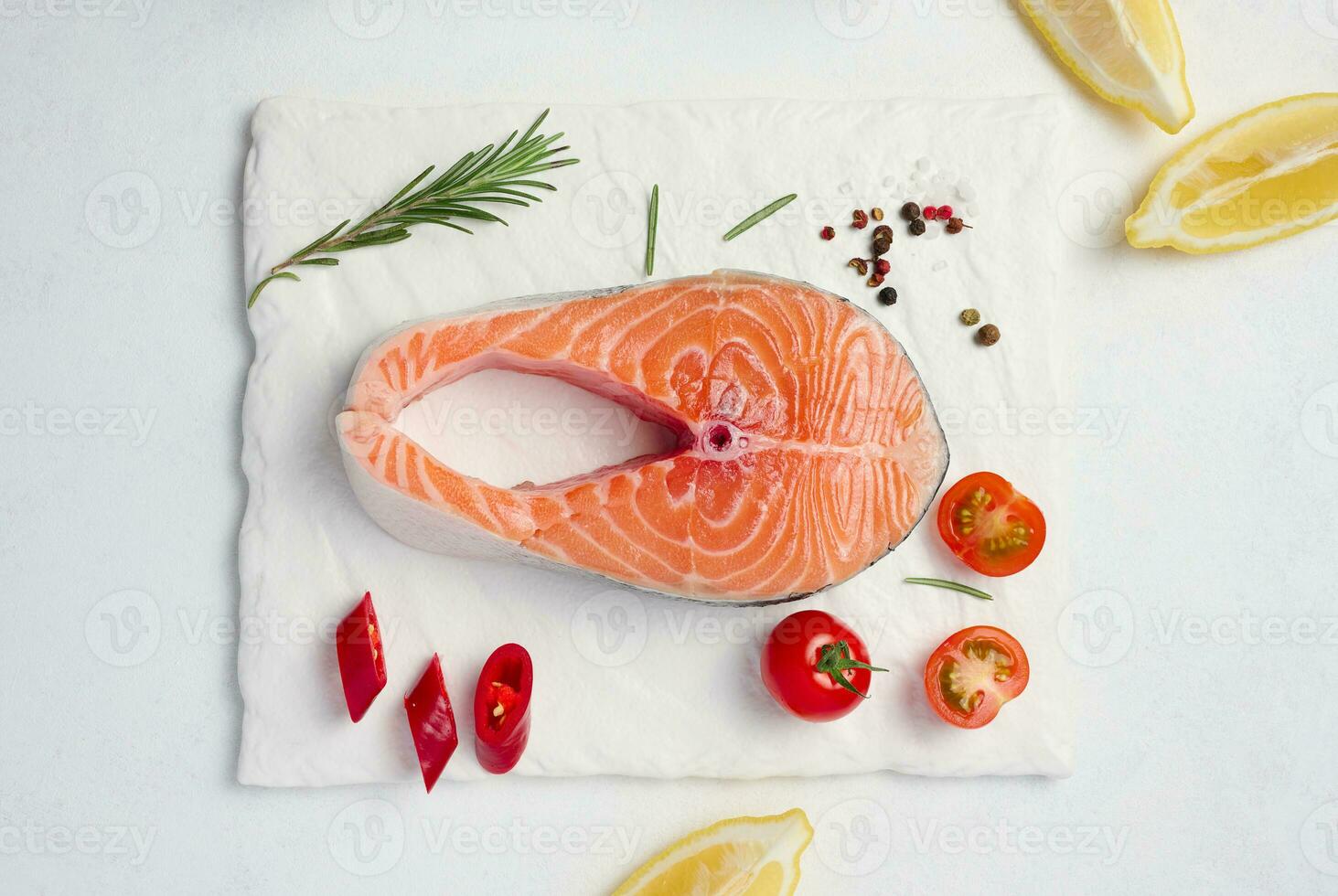 Raw piece of salmon, lemon slices and spices on a white board, top view photo