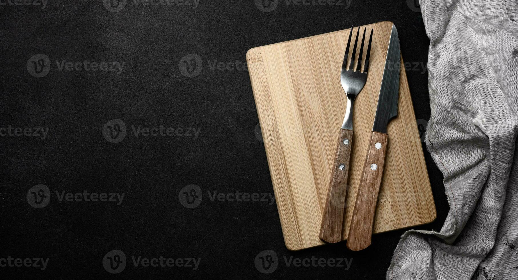 Fork and knife with wooden handle and cutting board on black background, top view photo