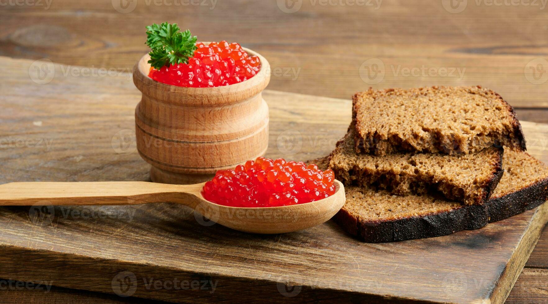 Red caviar in a wooden spoon, slices of bread on the table photo