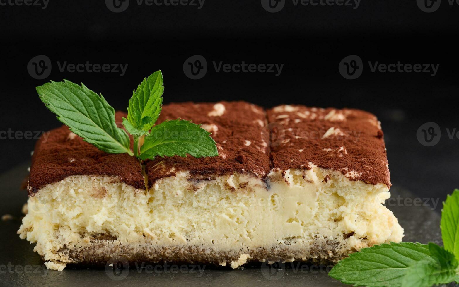 un pedazo de Tiramisu rociado con cacao, en parte superior de un puntilla de Fresco menta en un negro antecedentes foto