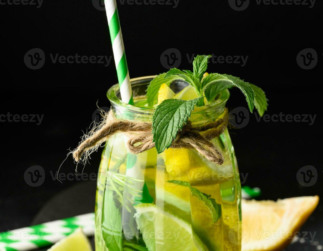 Lemonade in a transparent glass with lemon, lime, rosemary sprigs and mint leaves on a black background photo