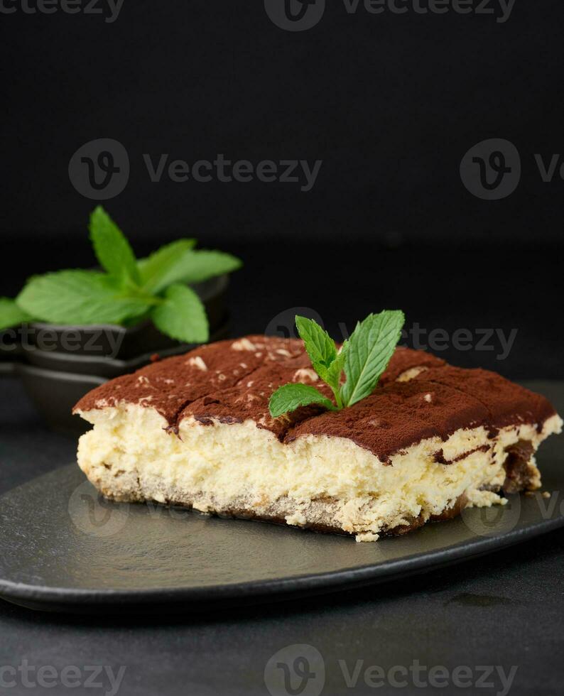 un pedazo de Tiramisu rociado con cacao, en parte superior de un puntilla de Fresco menta en un negro antecedentes foto