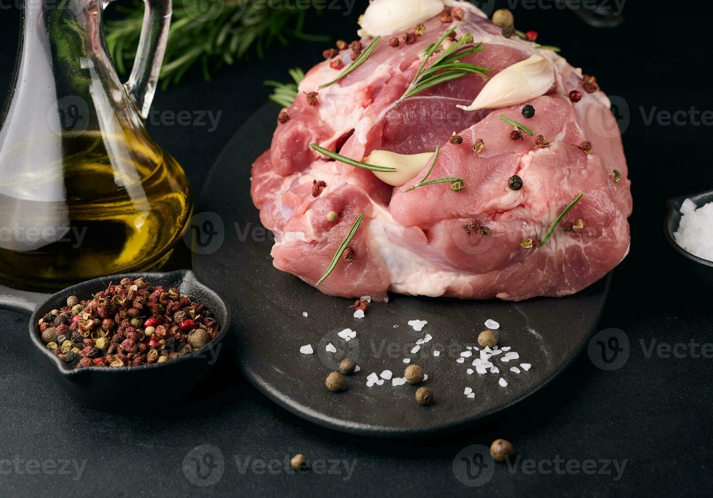 un pedazo de Cerdo jamón en un negro tablero y especias aceituna aceite, sal, Romero rama y pimienta foto