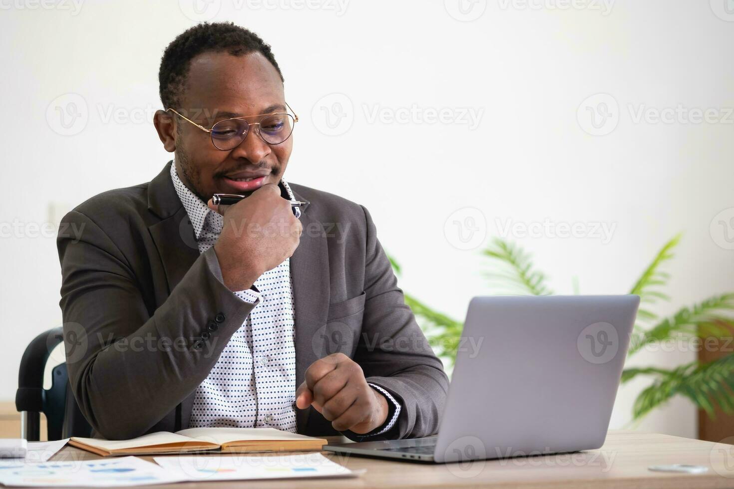 African American businessman analyzing laptop graph paperwork in office holding documents preparing portfolio analysis report Black male analyst doing paperwork in the workplace using the computer. photo