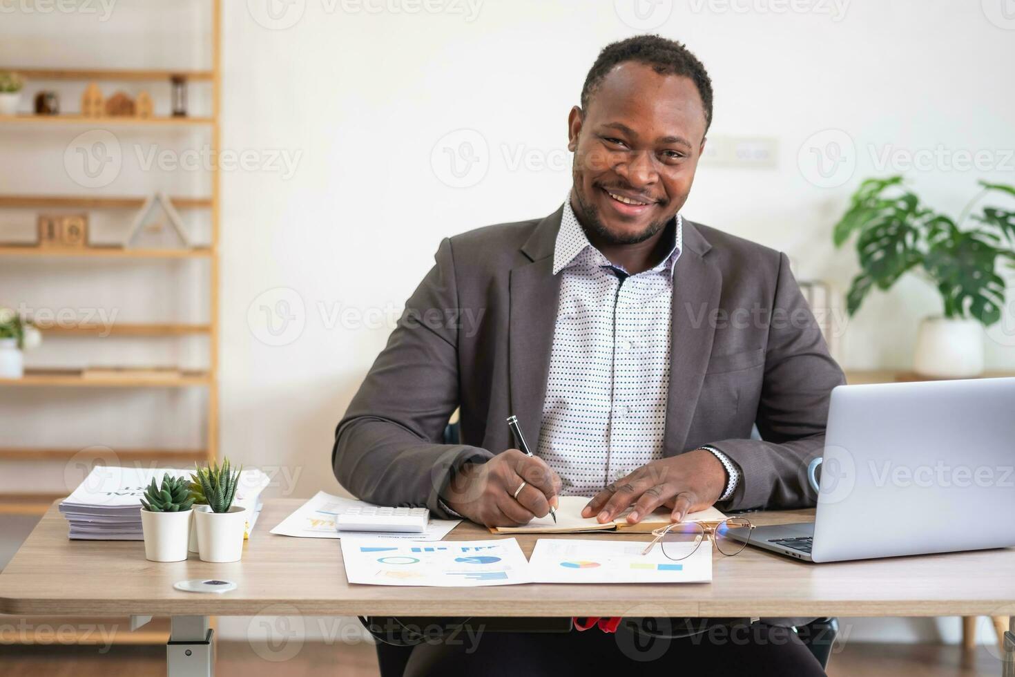 African American businessman analyzing laptop graph paperwork in office holding documents preparing portfolio analysis report Black male analyst doing paperwork in the workplace using the computer. photo