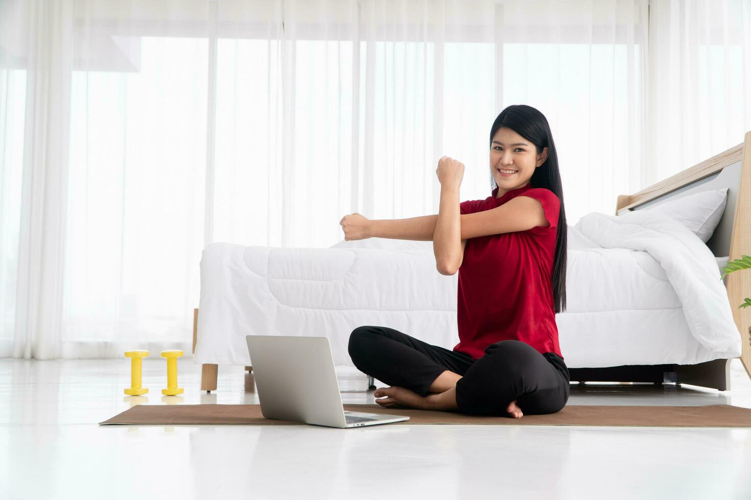 retrato de una joven asiática sana practicando ejercicios de yoga sentada en el dormitorio y aprendiendo en línea en una laptop en casa. concepto de ejercicio y relajación, tecnología para un nuevo estilo de vida normal foto