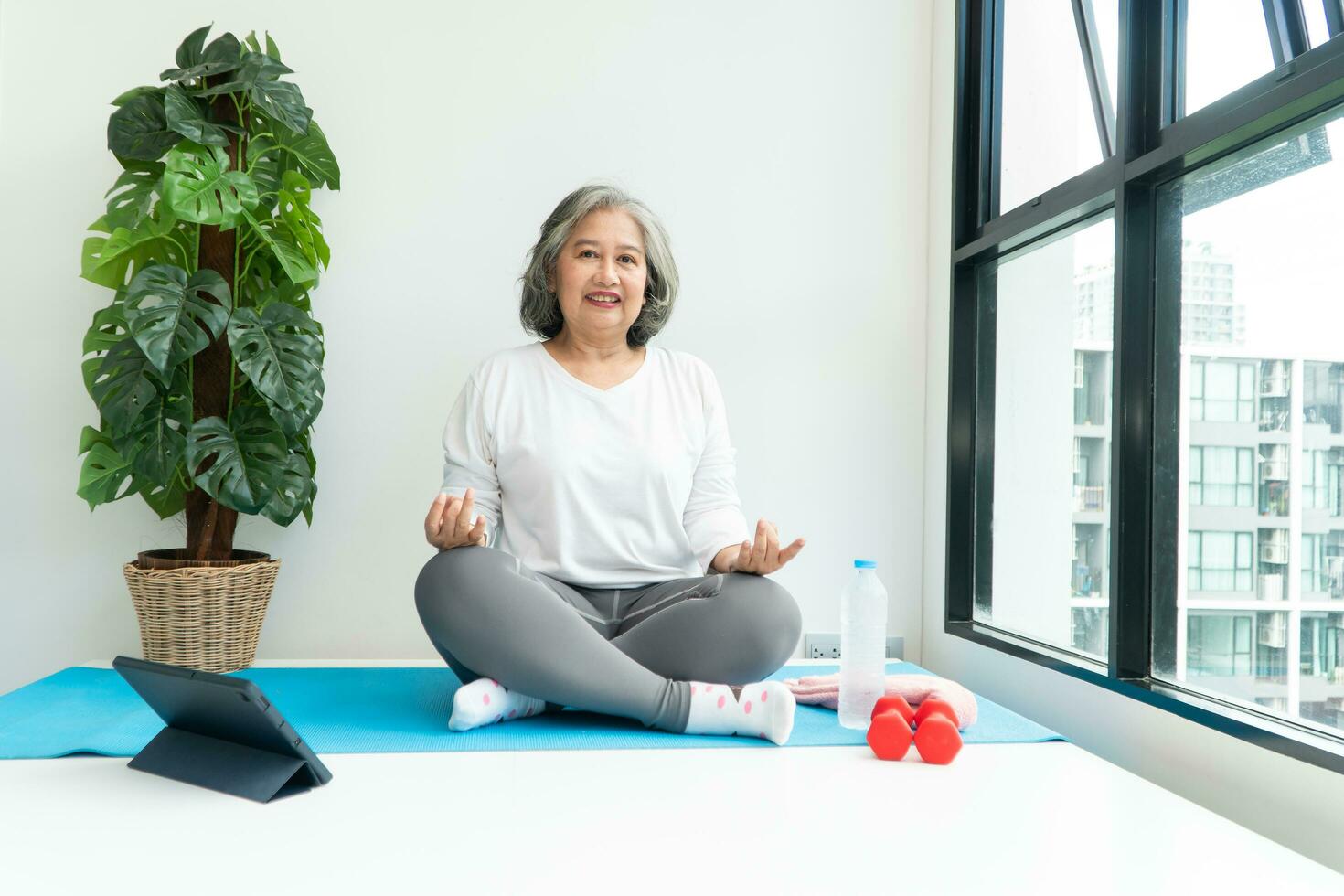 Senior Asian woman watching online courses on a laptop while exercising in the living room at home. Concept of workout training online. photo