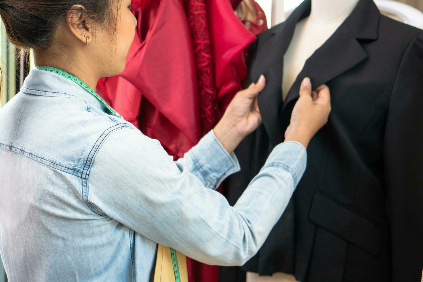 Happy young Asian woman dressmaker fashion designer is checking for completion for a suit and Dress in a showroom. Concept of success young entrepreneur in the fashion business. photo
