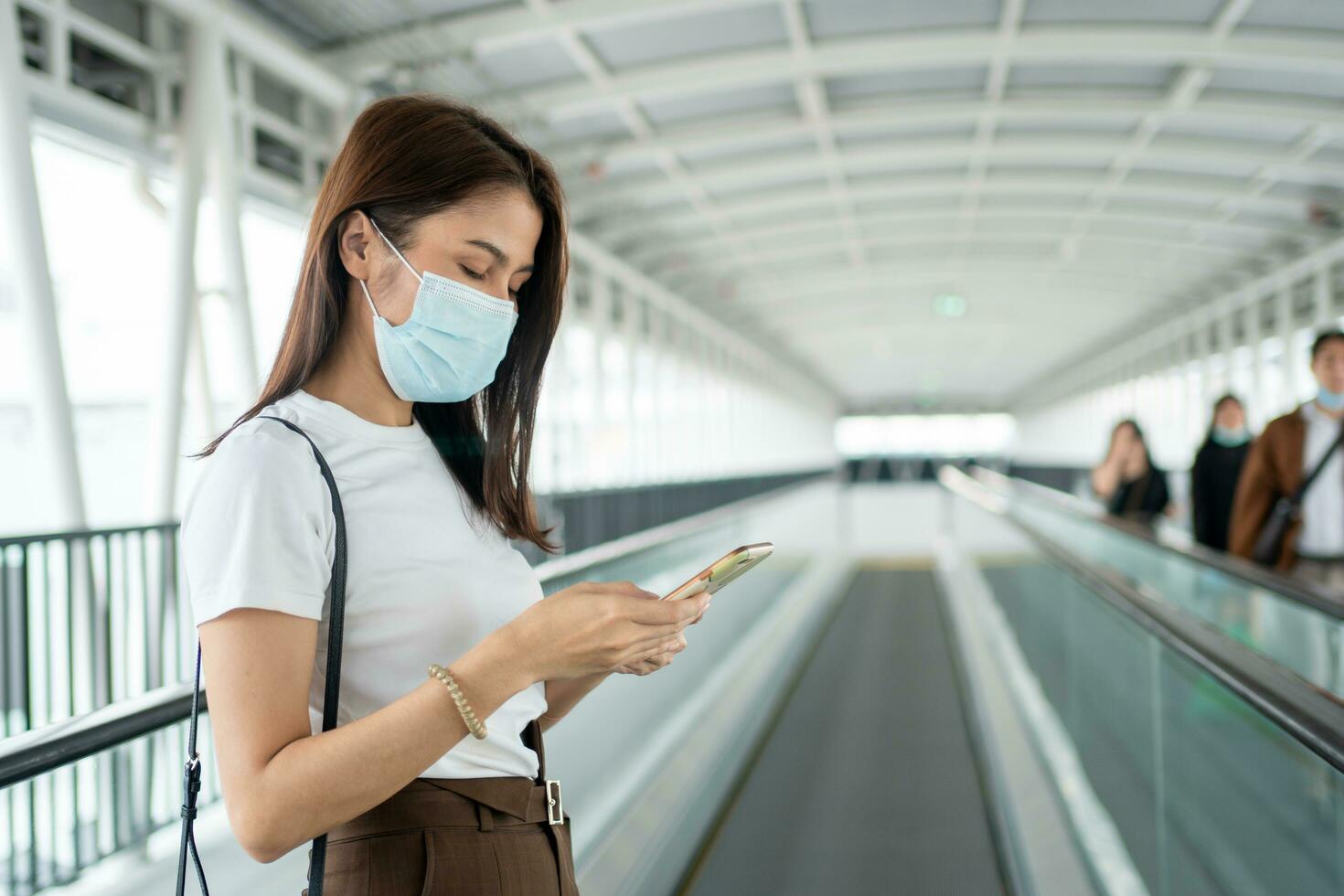 Portrait of a young woman in a medical mask for anti-coronavirus COVID-19 pandemic infectious disease outbreak protection and use a smartphone in Public area. Concept of Virus pandemic and pollution photo