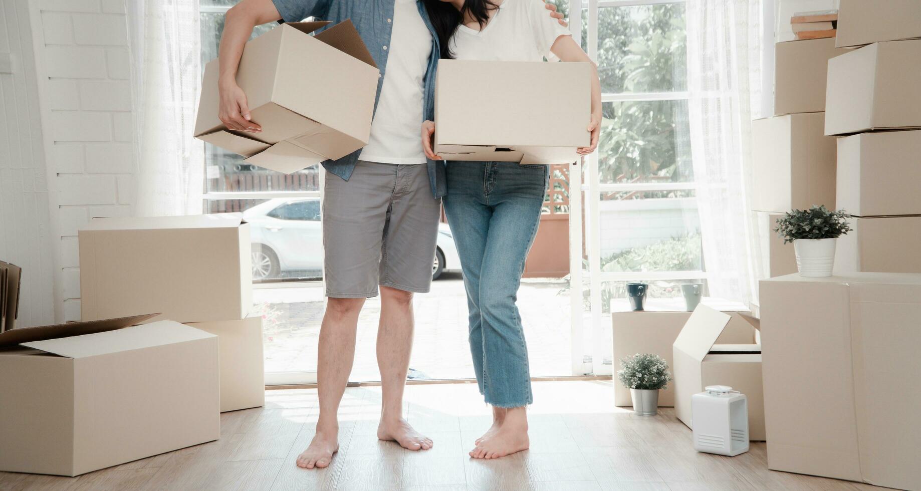 Happy young couple Carrying cardboard boxes and standing in the front door of a new house at moving day. Concept of relocation, rental, and homeowner moving at home. photo