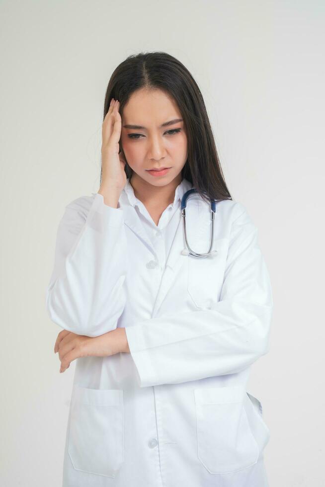 joven asiático mujer médico en pie y participación manos en el cabeza debido a dolor de cabeza, ella mira infeliz y cansado porque de trabajo excesivo, concepto de estresado y médico responsabilidad, relación comercial con frustrado foto