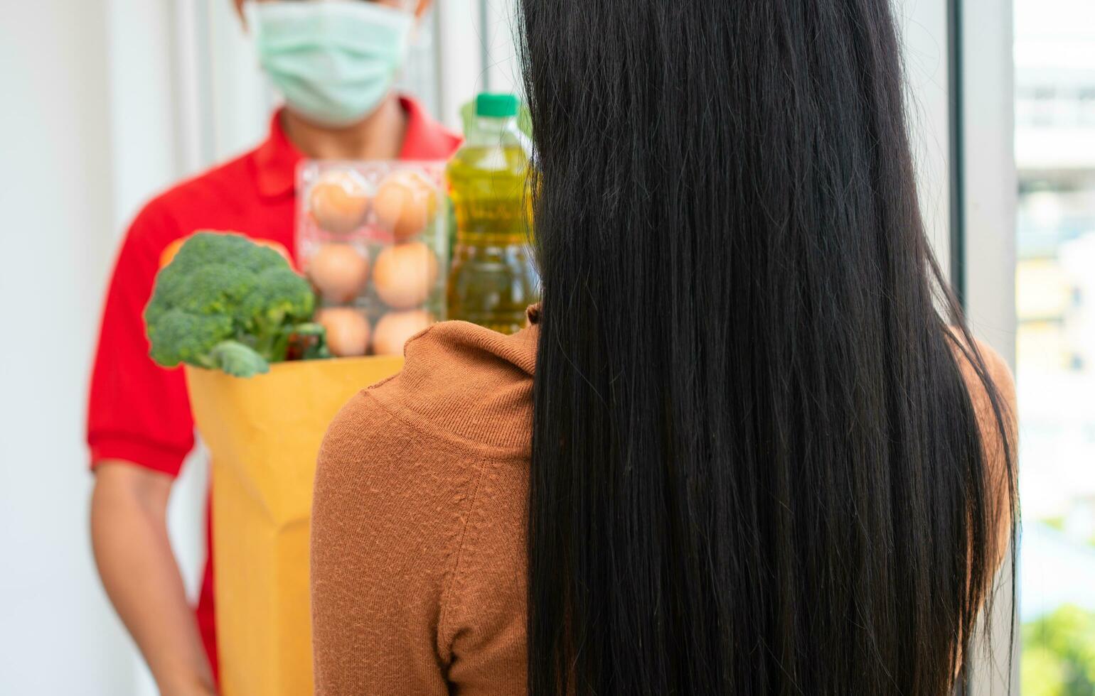 Asian delivery man from supermarket wearing a face mask and holding a bag of Fresh food, vegetables, and fruits for giving to customers at home. Concept of express grocery service and new  lifestyle photo