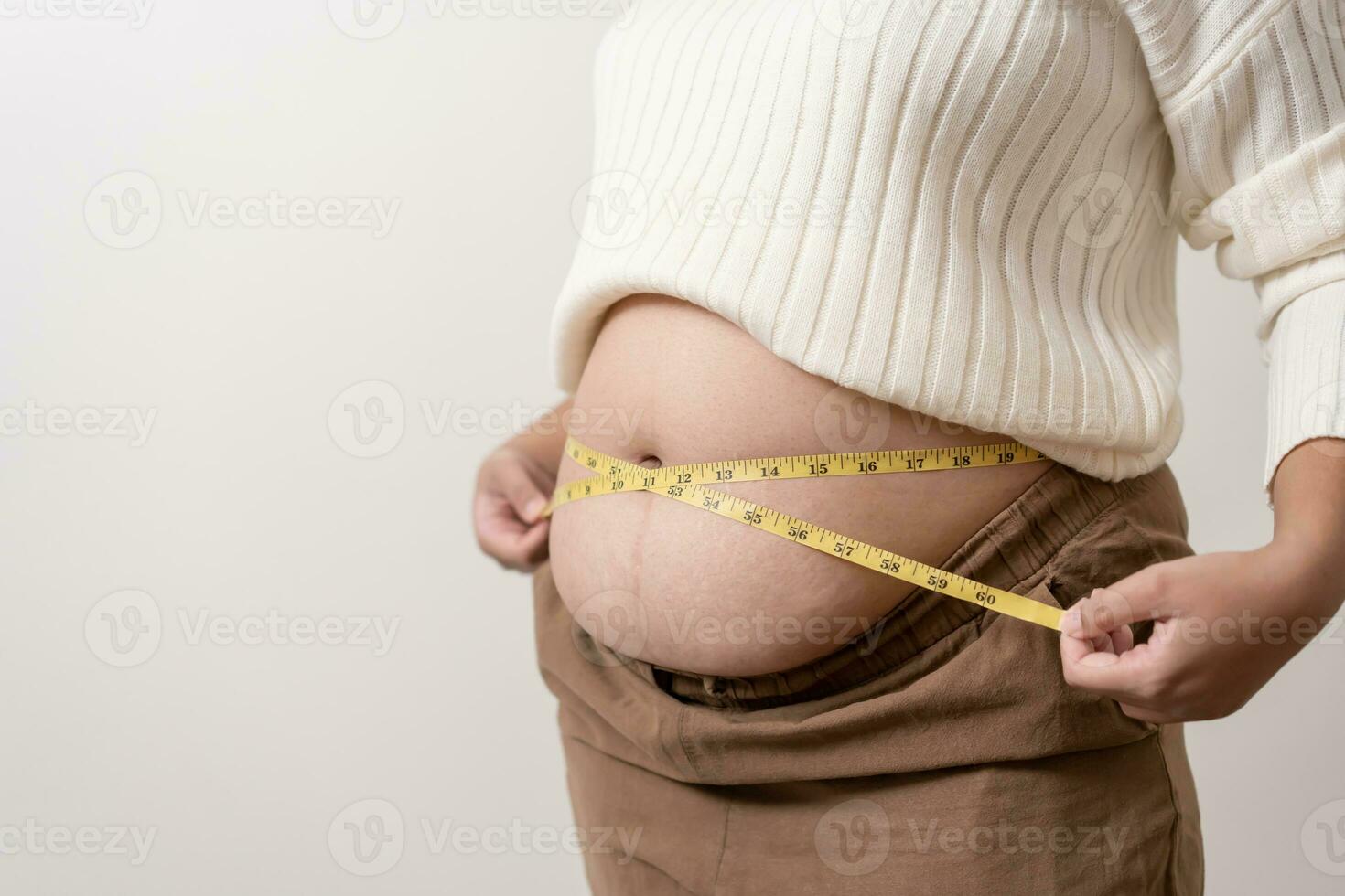 An obesity using measuring tape to show the real size. Chubby fat woman using measure tape at belly. photo