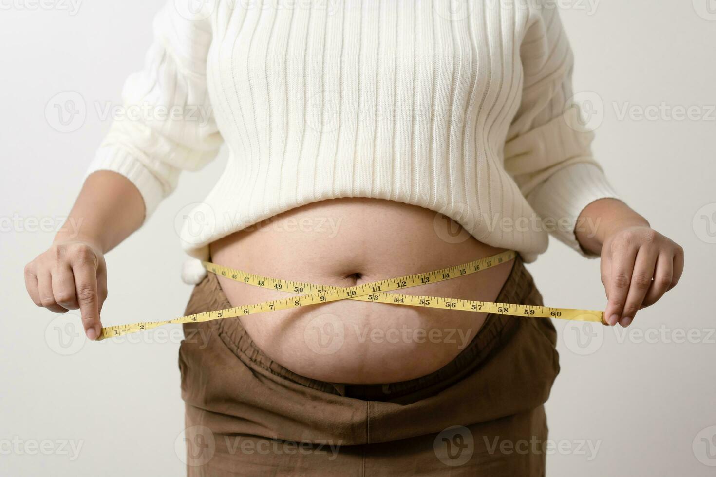 An obesity using measuring tape to show the real size. Chubby fat woman using measure tape at belly. photo