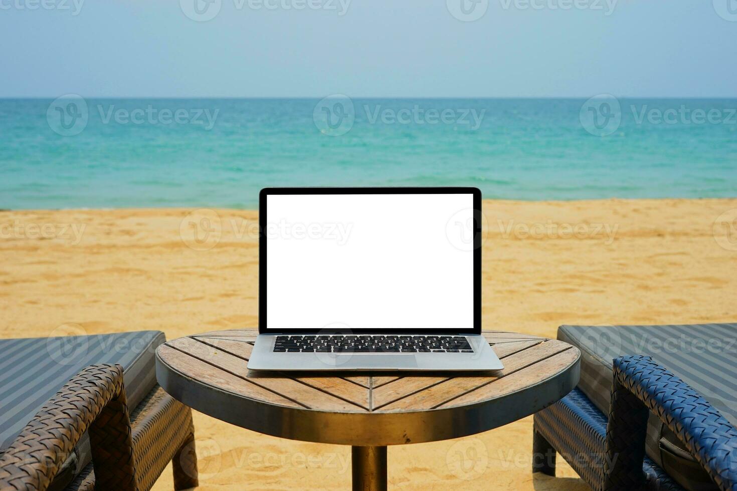 ordenador portátil con blanco pantalla para creativo diseño en el mesa cerca mar y arena playa antecedentes. computadora cuaderno con monitor recorte camino para presente aterrizaje página diseño burlarse de arriba modelo foto