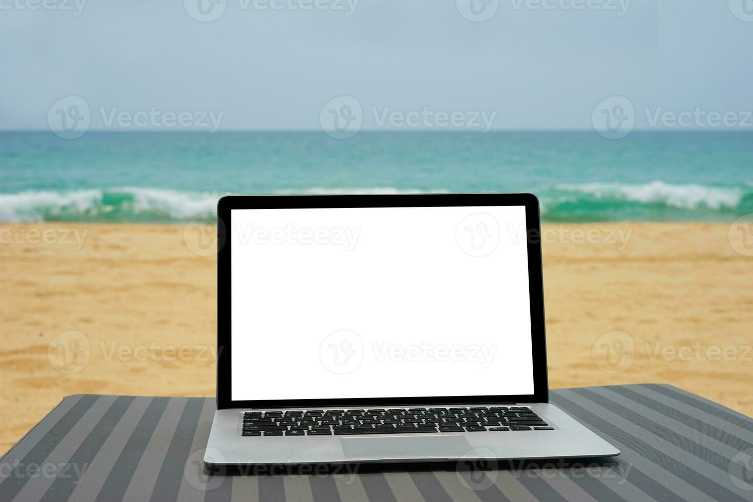 ordenador portátil con blanco pantalla para creativo diseño en playa cama cerca playa y azul mar antecedentes. computadora cuaderno con recorte camino para presente aterrizaje página diseño burlarse de arriba modelo foto