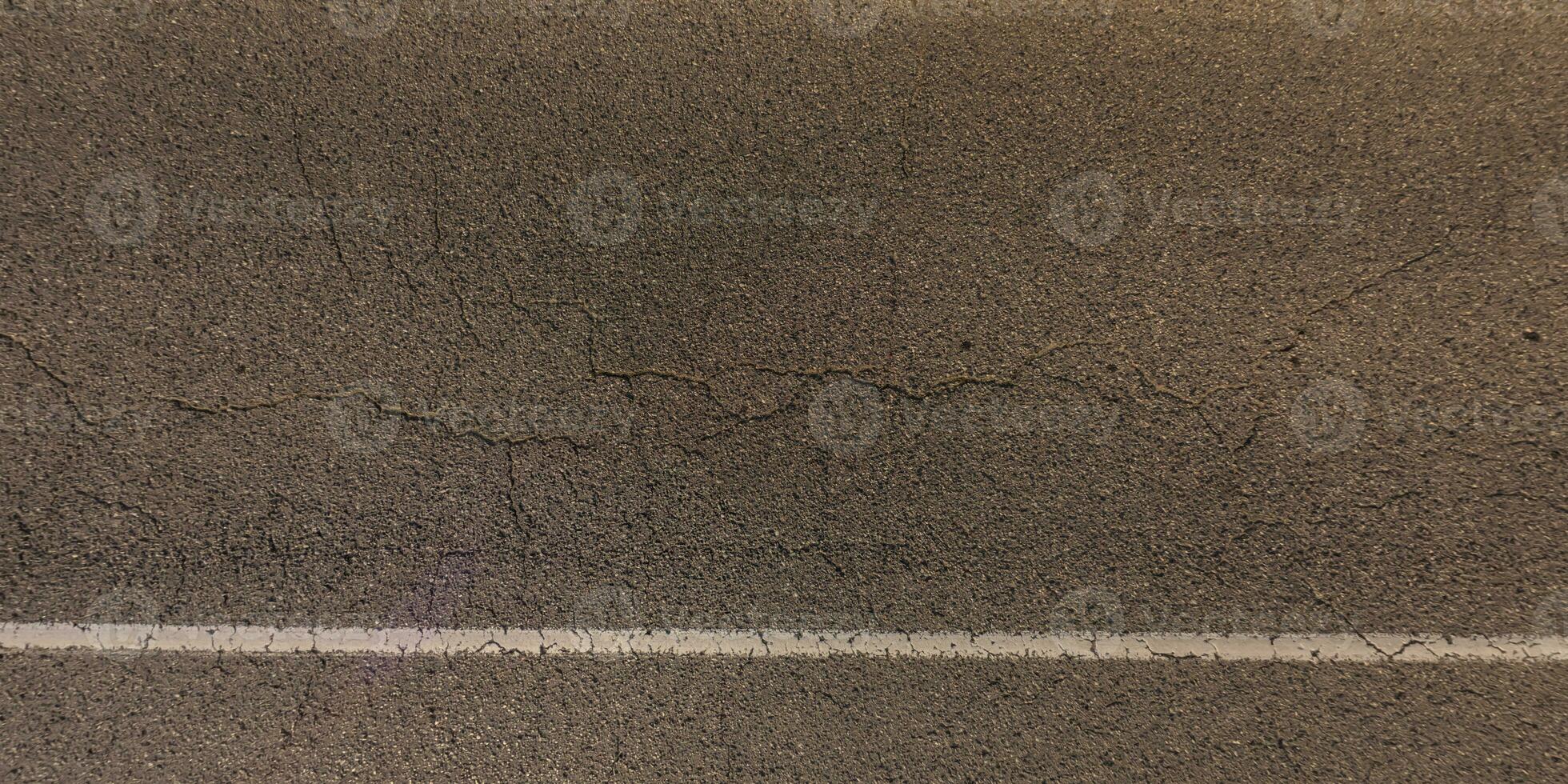 top view of surface of asphalt road made of small stones and sand with cracks photo