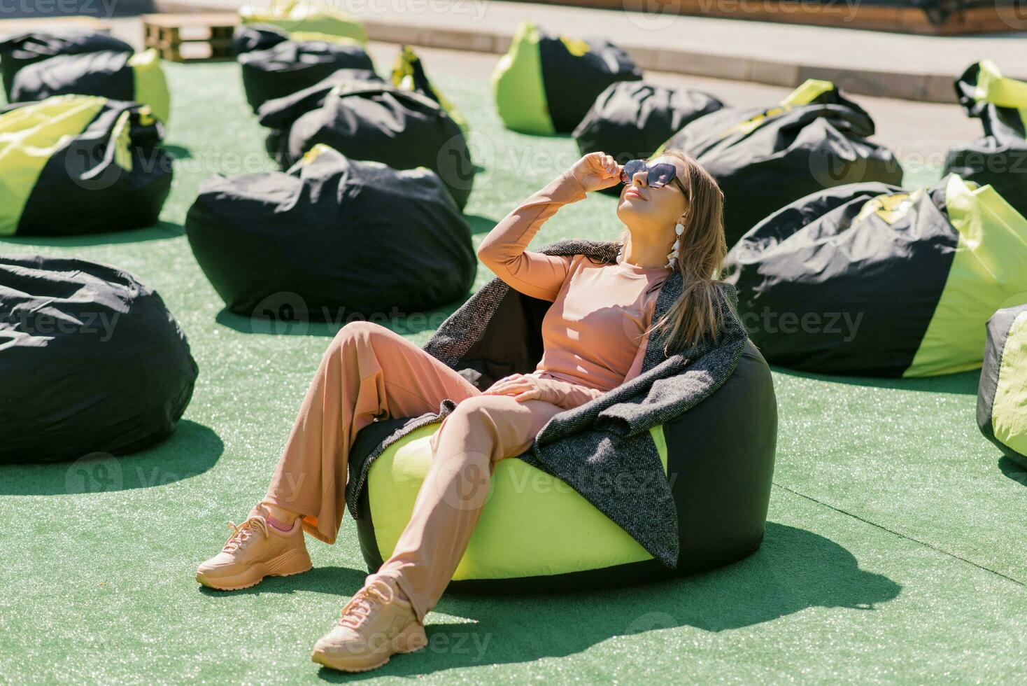 bonito blanco joven mujer es acostado en un fácil silla en el abierto aire vistiendo Gafas de sol y sonriente. el concepto de descanso y relajación. foto