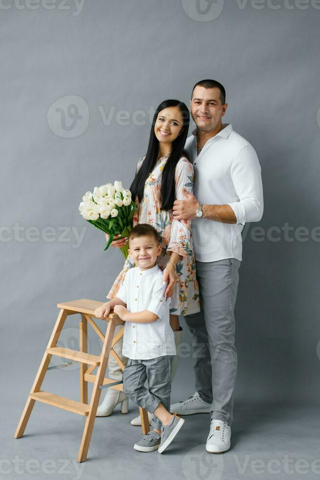 Stylish young family, mom, dad and four-year-old son stand near a wooden stepladder and smile, isolated on a white background. Happy family photo