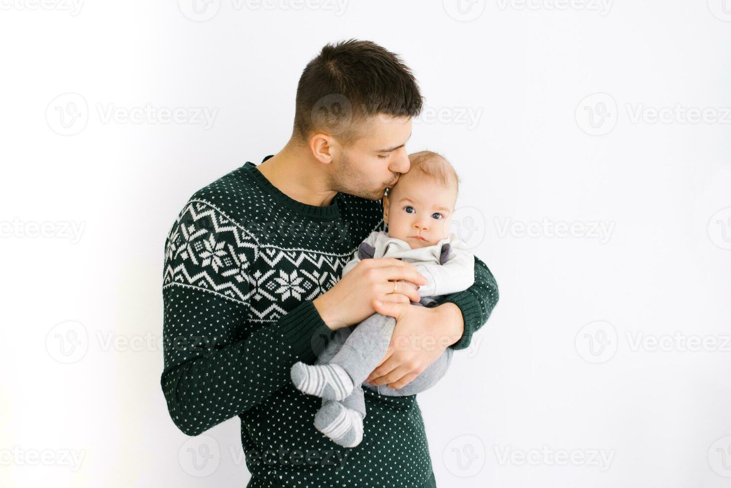 un joven padre sostiene su pequeño hijo en su brazos y Besos él en un blanco antecedentes foto