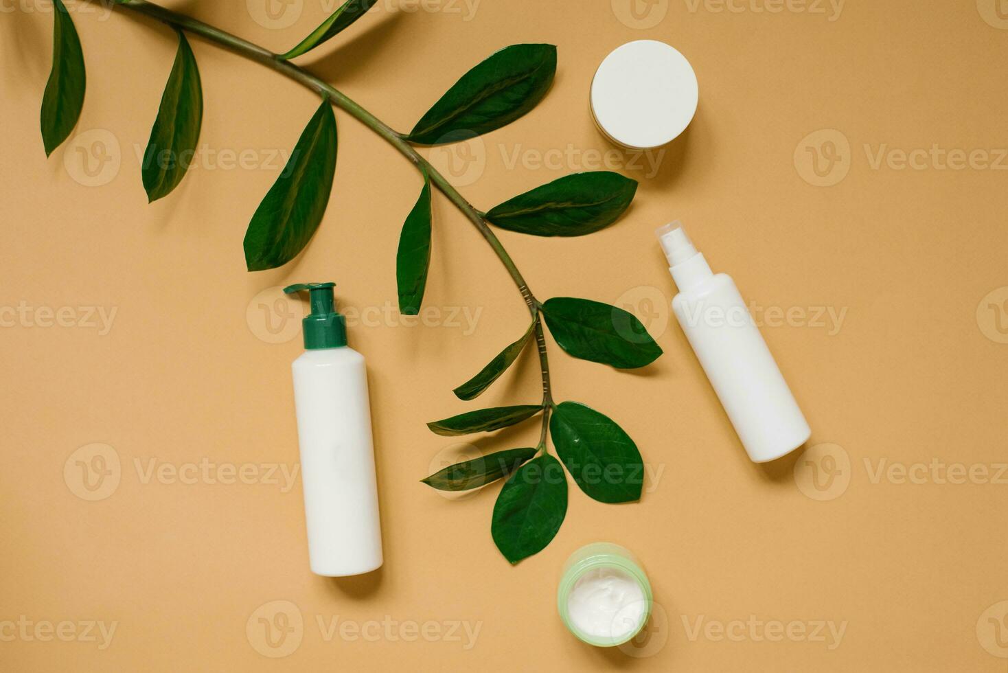 Natural herbal creams in bottles and jars with green leaves on a beige background. The concept of a natural organic cosmetic product. Flat position, top view. photo