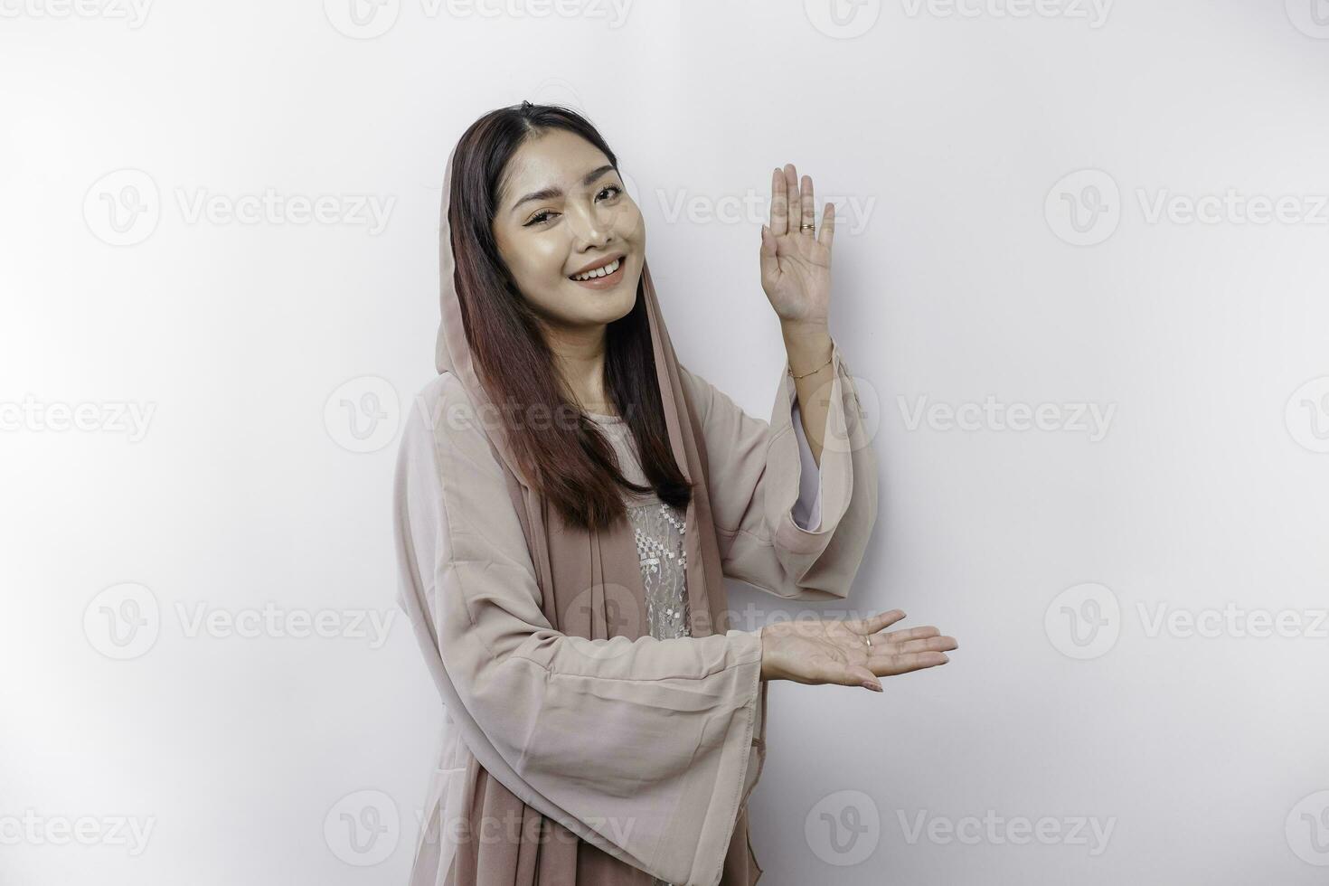 Young Asian Muslim woman smiling while pointing to copy space beside her photo