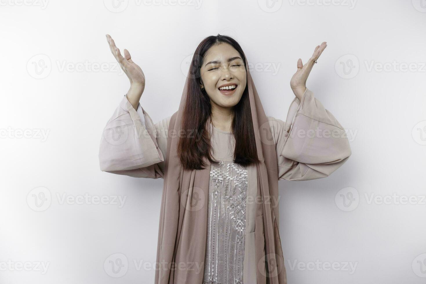 Excited Asian Muslim woman wearing headscarf pointing at the copy space above her, isolated by white background photo