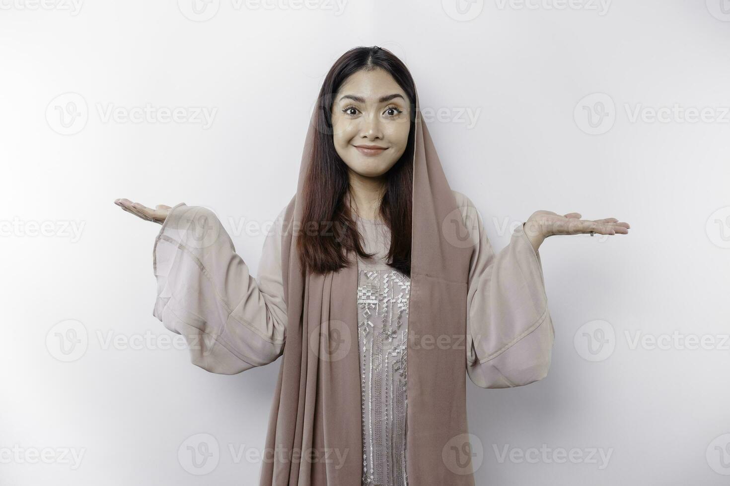 Young Asian Muslim woman smiling while pointing to copy space beside her photo