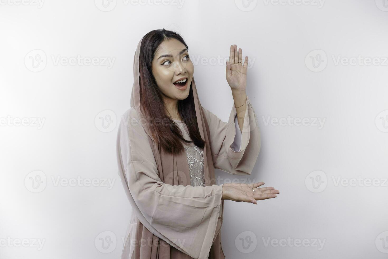 Shocked Asian Muslim woman pointing at the copy space on beside her, isolated by white background photo