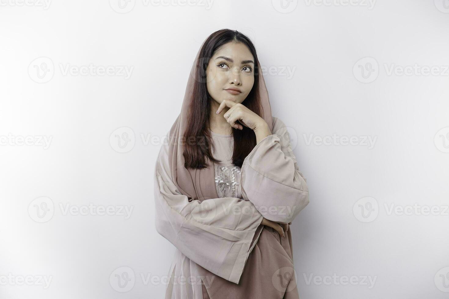 A thoughtful young Asian Muslim woman wearing headscarf while looking aside, isolated by a white background photo