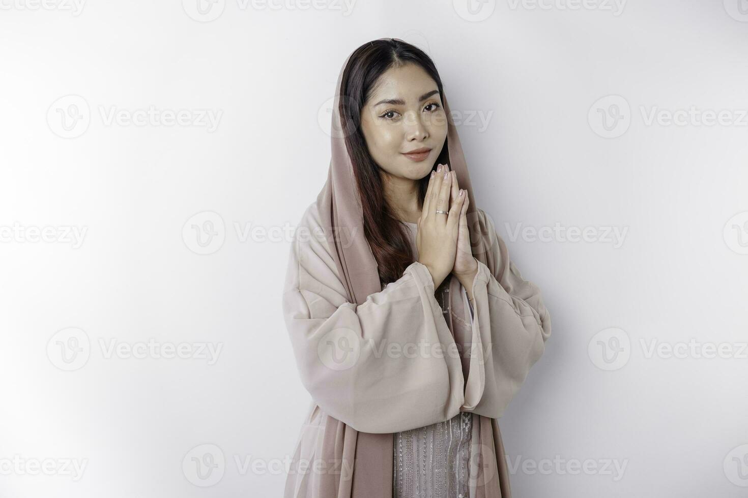 Religious beautiful Asian Muslim girl wearing a headscarf praying to God, isolated by white background photo