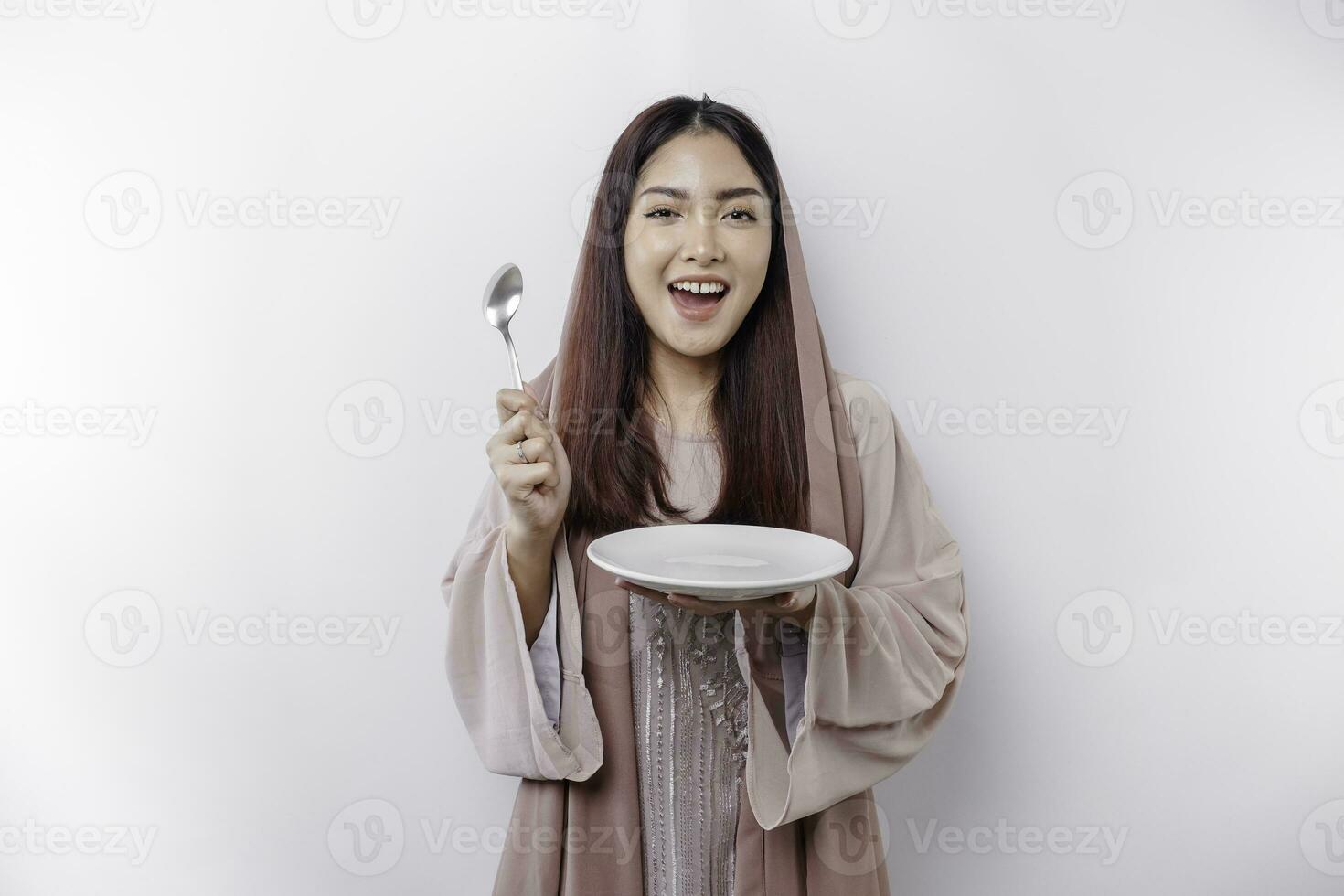 An Asian Muslim woman is fasting and hungry and holding cutlery while looking aside thinking about what to eat photo