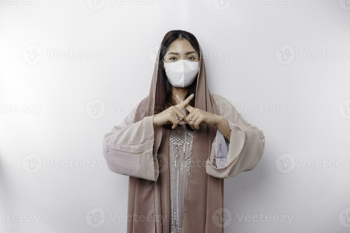 A cautious Asian Muslim woman wearing a mask as a preventive for covid-19 with hand gesture pose rejection or prohibition photo