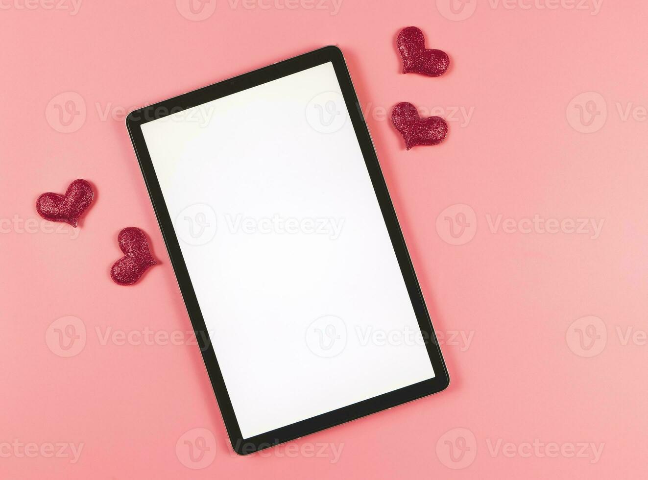 flat lay of digital tablet with blank white screen, red glitter hearts  isolated on pink background. photo