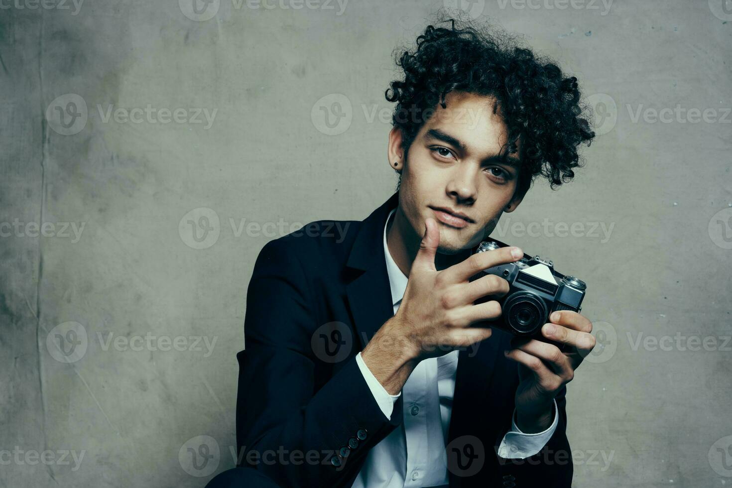 curly-haired man in a classic suit looks at the camera in his hand studio hobby photo