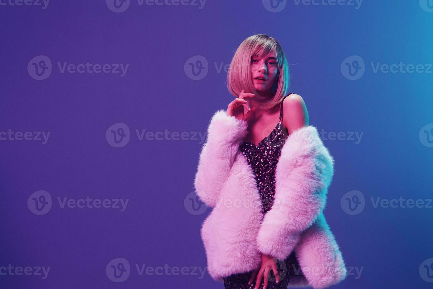 Cool fashion offer. Pretty adorable blonde woman in fluffy fur coat sparkly dress posing isolated in blue violet pink color light studio background. Neon party concept. Copy space Banner photo