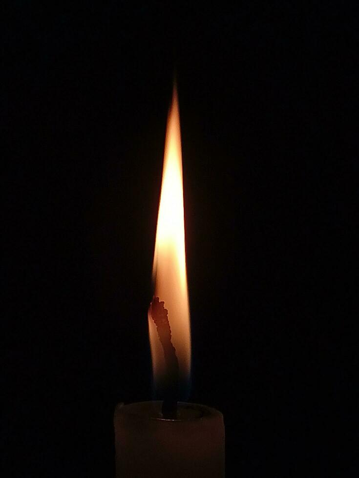 A candle with a flame is lit up in the dark. photo