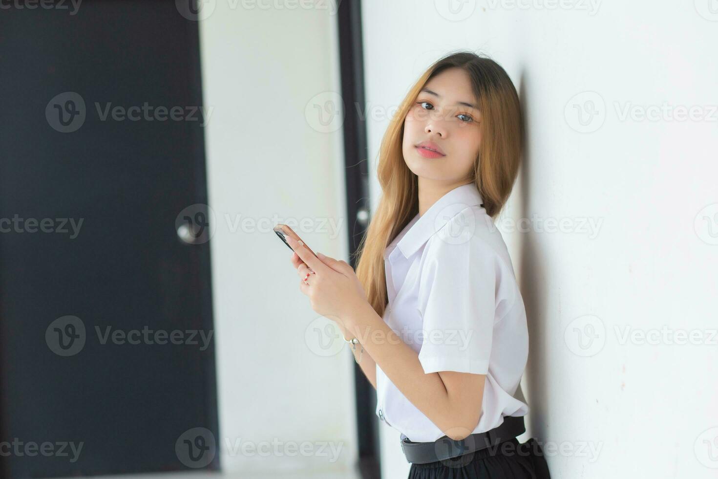 Portrait of cute Asian Thai girl student in a uniform is smiling happily while using a smartphone at university. photo