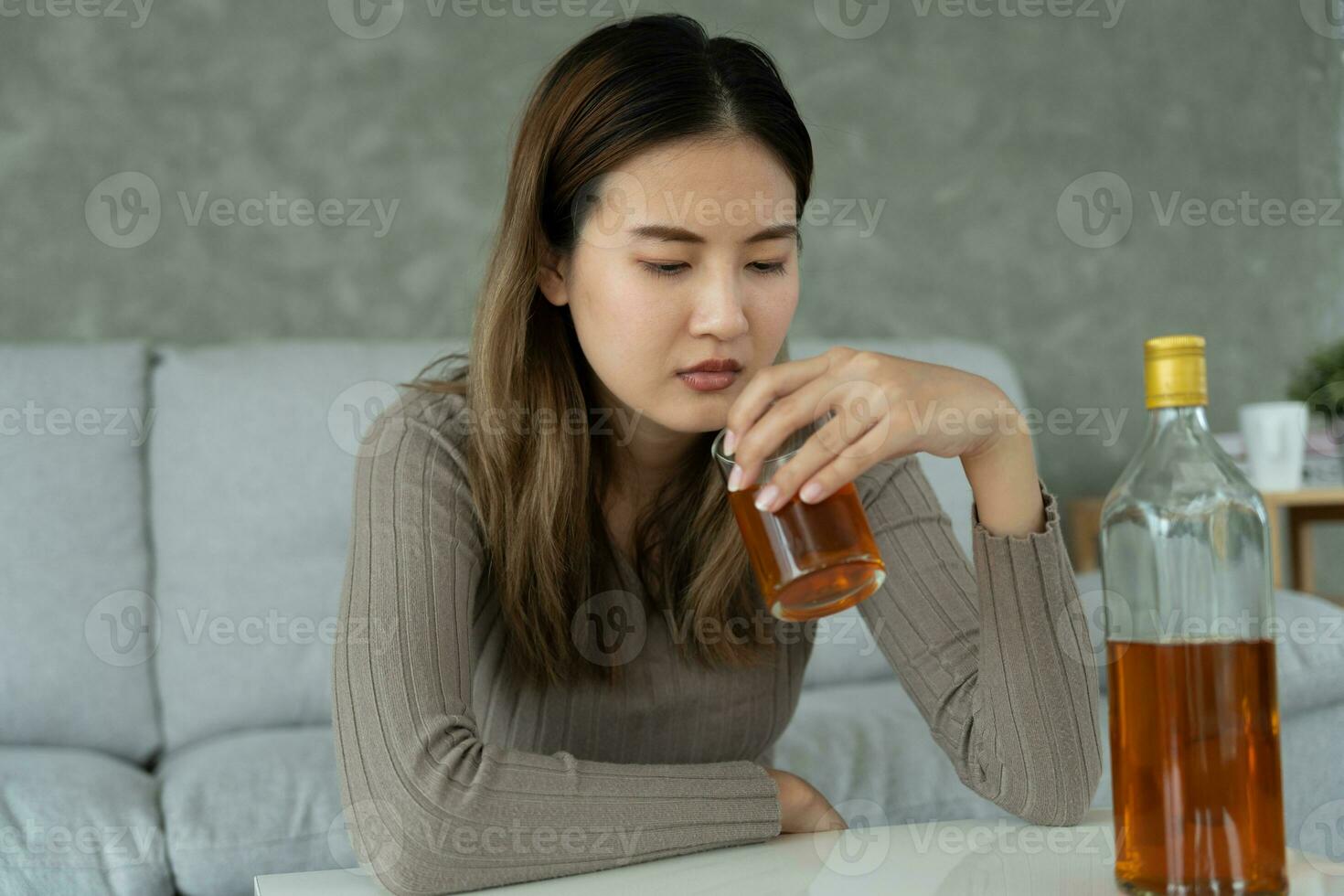 Depressed young Asian woman addicted feeling bad drinking whiskey alone at home, stressed frustrated lonely drinking alcohol suffers from problematic liquor, alcoholism, life and family problems photo