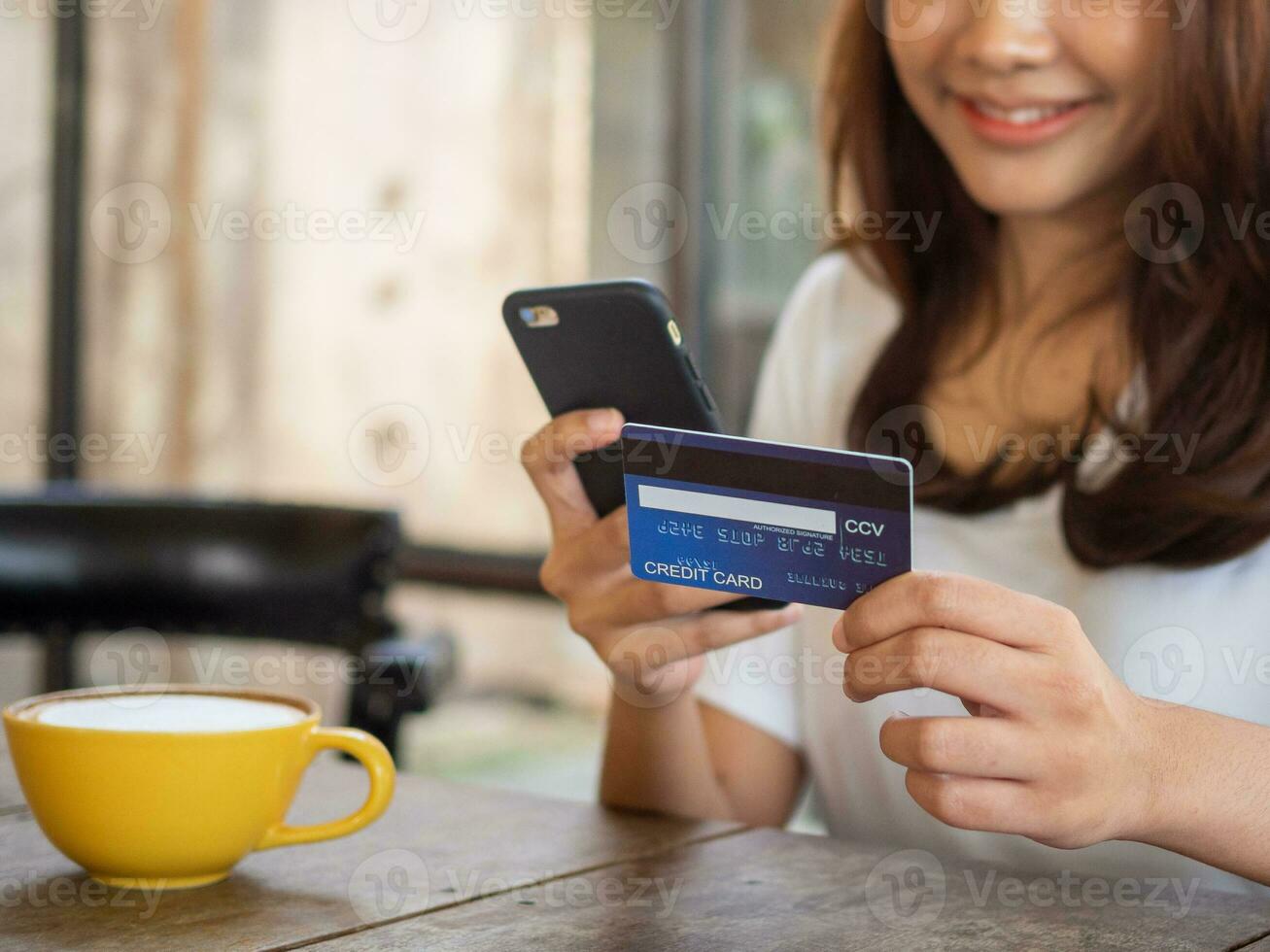 The smiling young Asian woman enjoys shopping online via a smartphone and paying online via credit card. Convenience of spending without cash. photo