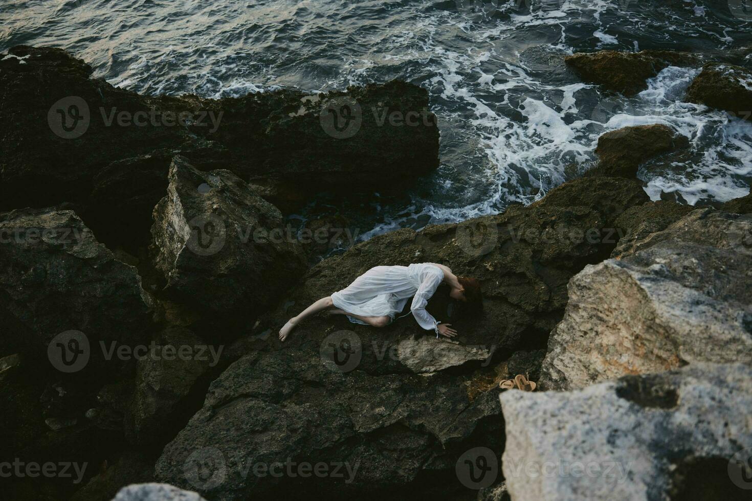 beautiful young woman in long white dress wet hair lying on a rocky cliff Summer vacation concept photo