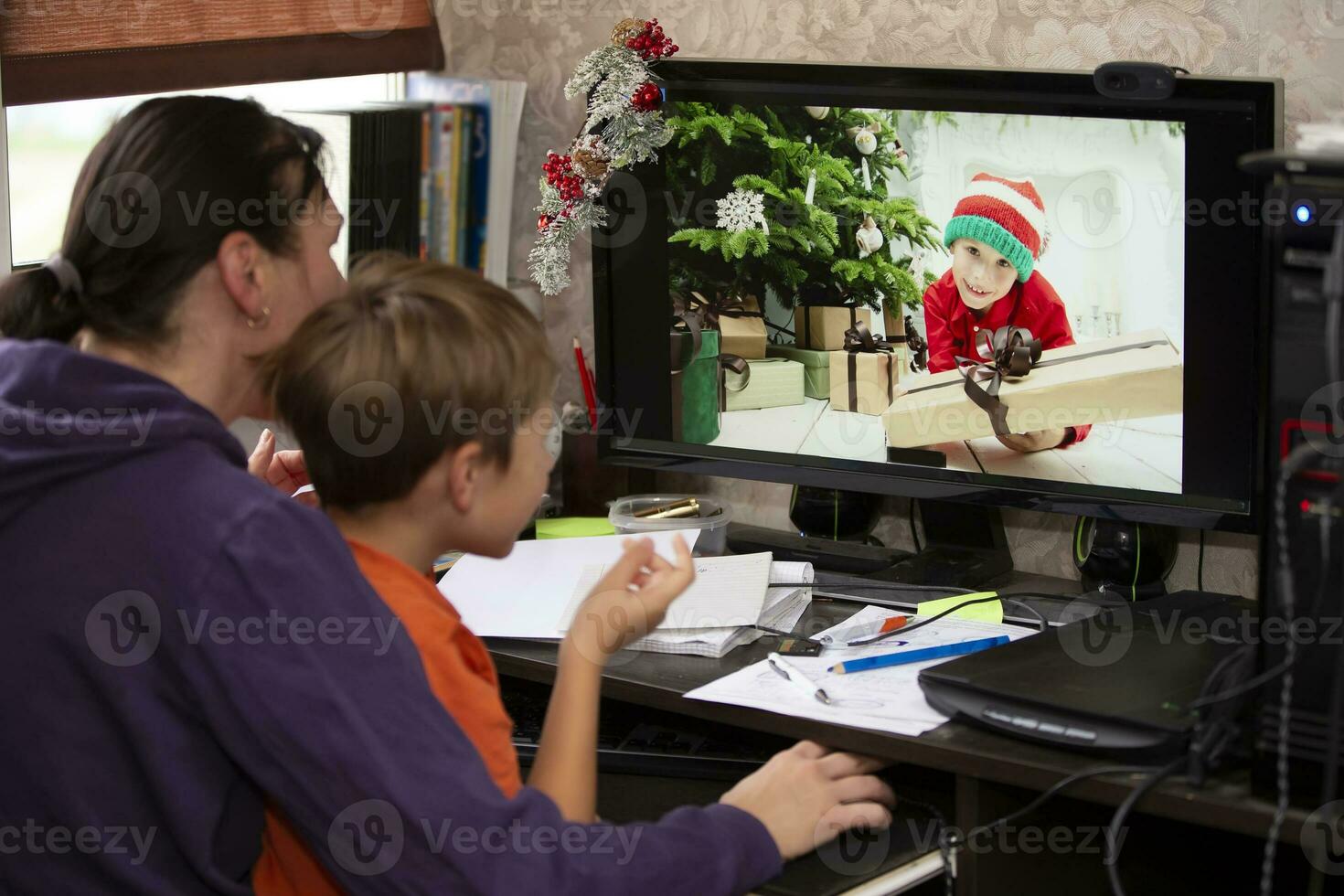 The woman and the child are sitting at the table and talking via video link with the boy on the computer. Staying at home, quarantine and social distancing during the New Years. photo