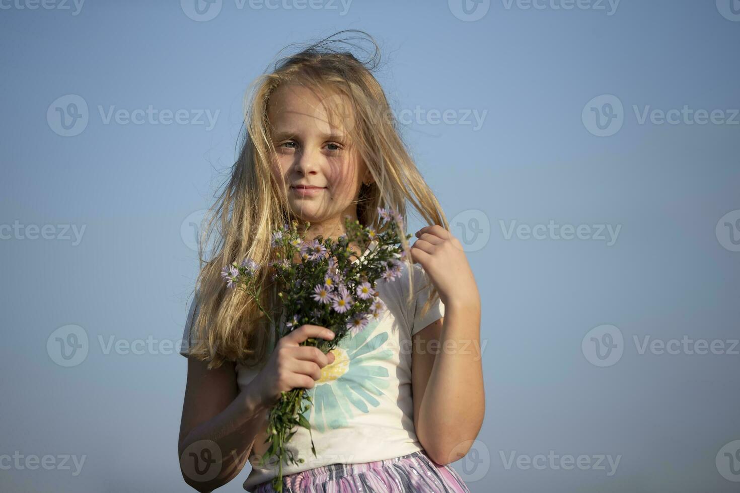 Beautiful little girl with a bouquet of wild flowers against the sky. photo