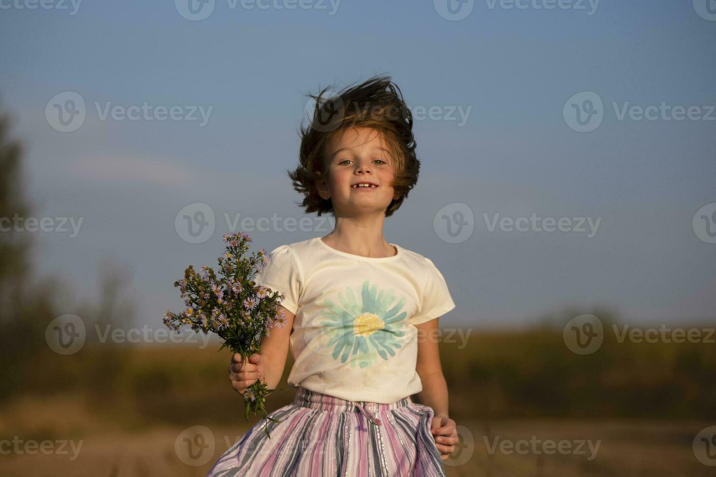 Happy little girl in the meadow with a bouquet of flowers. A child on a beautiful summer field with developing hair. photo