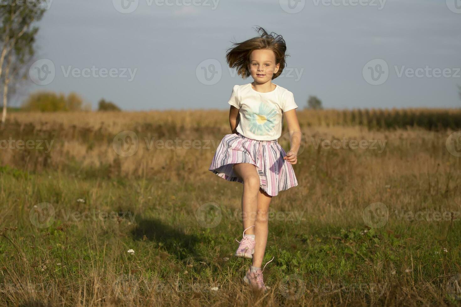Beautiful little girl runs in the summer field. The child plays in the meadow. photo