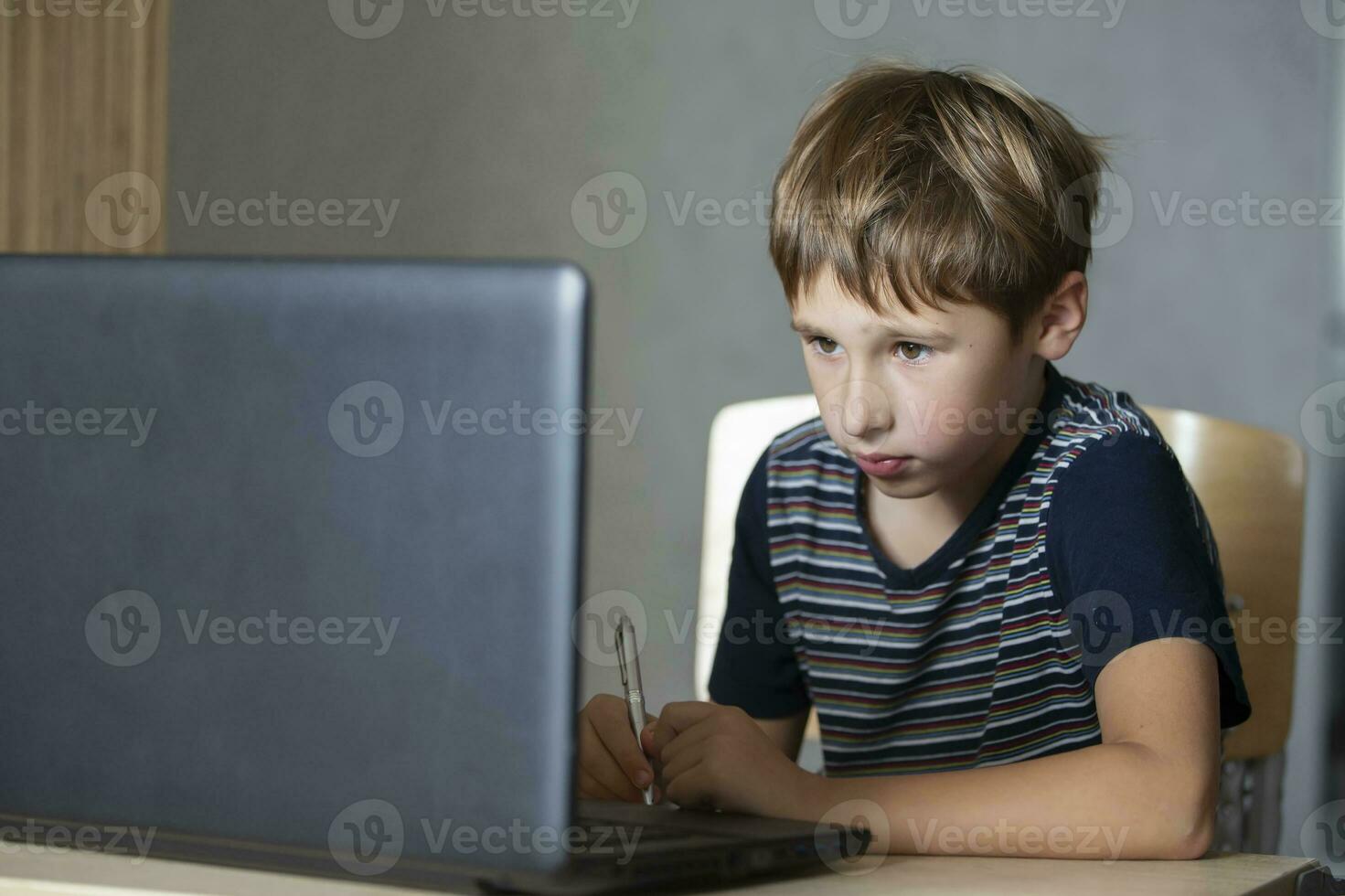 Schoolboy during online lesson at home, social distance during quarantine, self-isolation, online education concept. Elementary age boy at laptop at home. photo