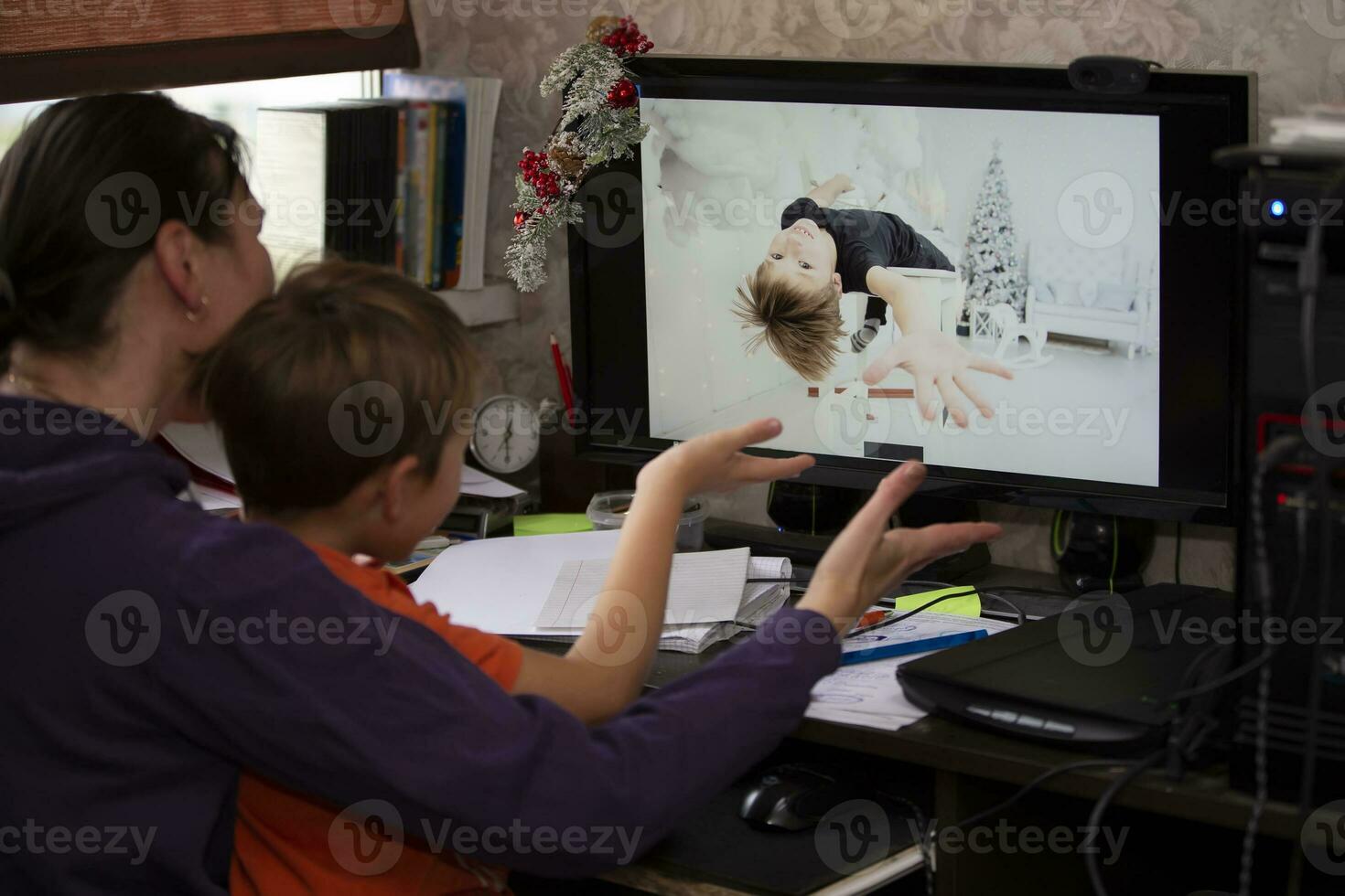 A woman and a child are sitting at a table and talking via video link with a boy relative or friend. Staying at home, quarantine and social distancing during the New Years. photo
