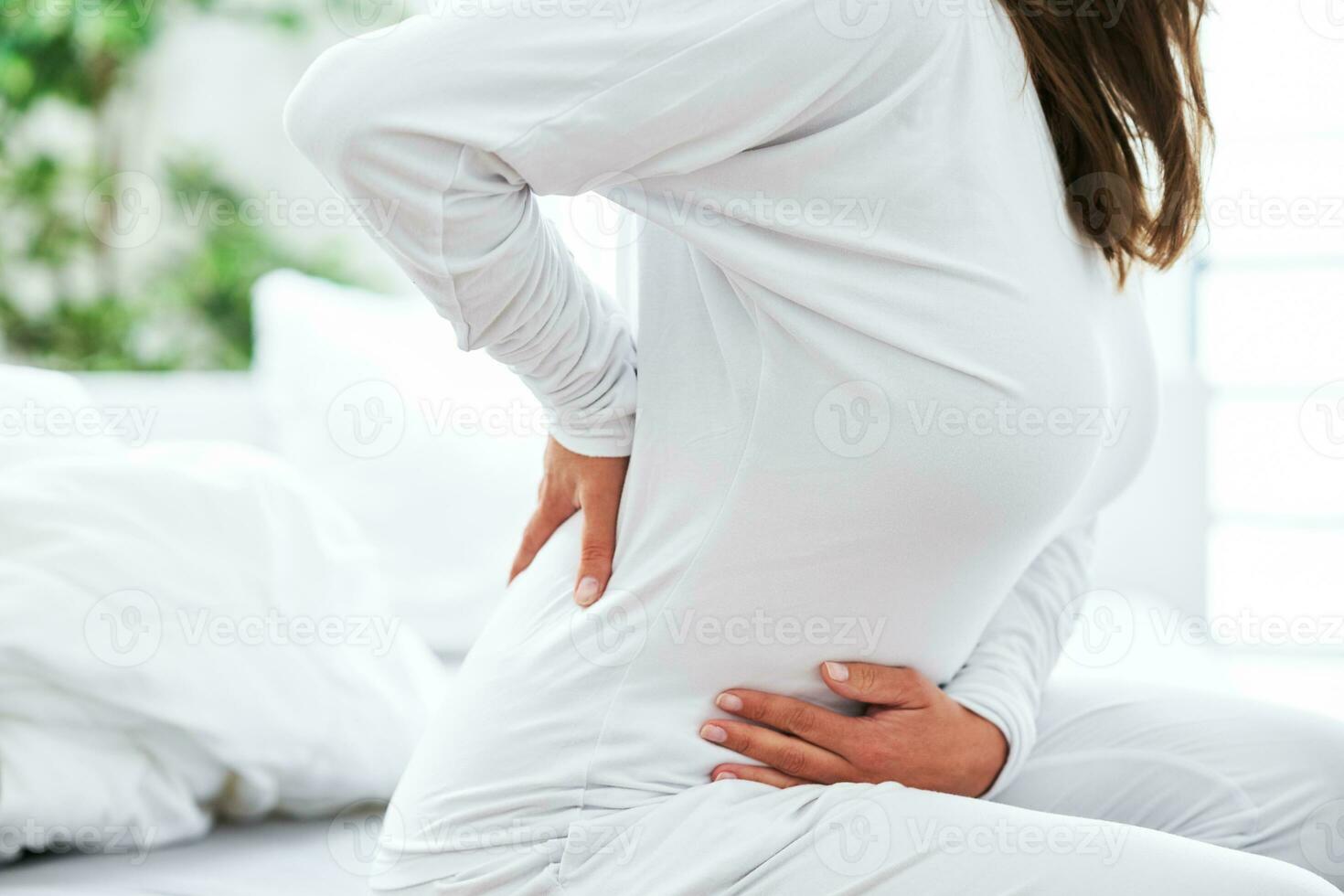Young brunet woman withe her back problem in the bed photo