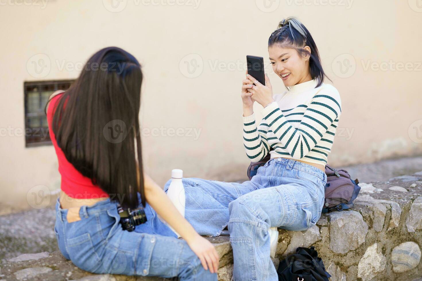 Smiling Asian woman taking picture of girlfriend on street photo